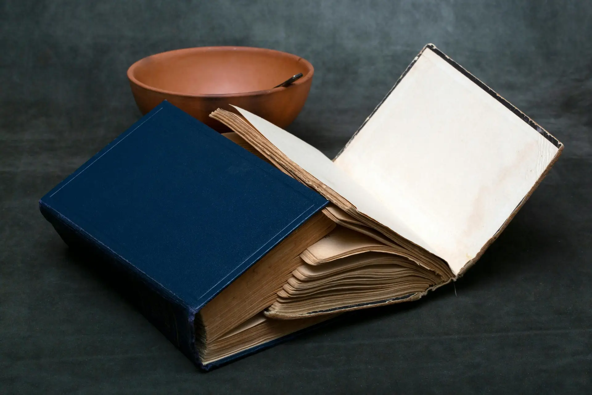 An open vintage book lies next to a clay bowl, creating a rustic and scholarly ambiance.